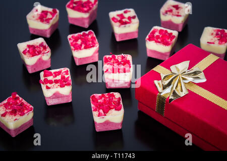 Geschenk verpackt in rotem Papier mit Gold Ribbon in Bogen mit feiner Schokolade mit roten besprüht gebunden. Geburtstag Geschenk oder für Valentines Tag. Stockfoto