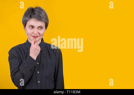 Verträumt kaukasisch Weiblich mit nachdenklichen Ausdruck schaut weg, hält den Finger in der Nähe von Lippen, denkt an etwas Schönes, trägt schwarze Shirt Posen gege Stockfoto