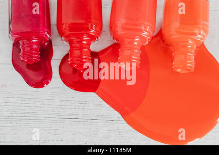 Nagellack Flaschen in verschiedenen Nuancen von Rot zu Orange und Lila verschütten Farbe auf Holz- Oberfläche, Konzept der Kosmetikindustrie und Maniküre Stockfoto