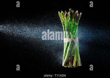 Spargel in Spritzer auf schwarzem Hintergrund. Close-up. Eine Reihe von Obst und Gemüse in Bewegung. Stockfoto