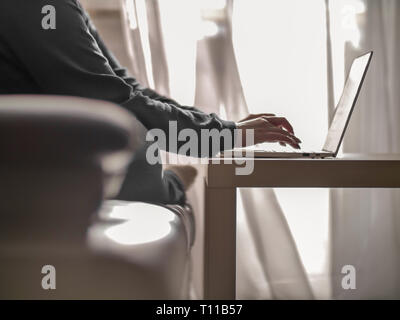 Frau Texteingabe auf einem Laptop beim Sitzen auf einem Sofa Stockfoto