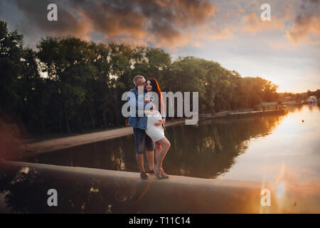 Familie warten auf ein Baby stehen durch den Fluss bei Sonnenuntergang. Stockfoto