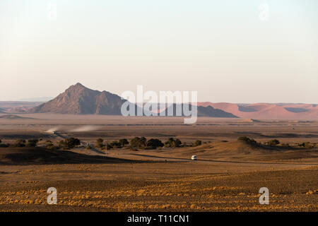 Autos heben Staub auf dem Weg durch die Namib Naukluft National Park zu den berühmten roten Dünen im Sossusvlei, Namibia. Stockfoto