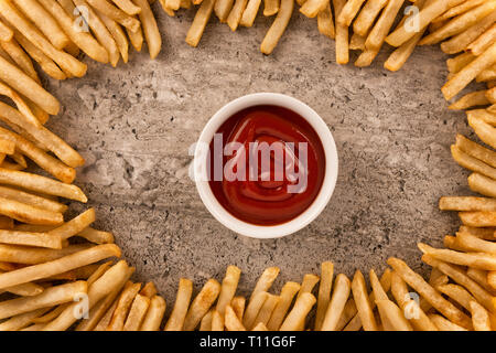 Grenze von Pommes Frites mit Ketchup in der Mitte auf konkreten Hintergrund isoliert, direkt oberhalb. Close Up. Stockfoto