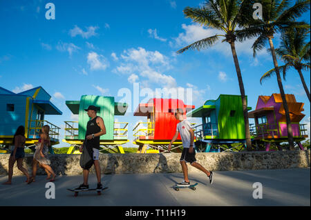 MIAMI - Juli 2017: Junge Männer auf skateboards Pass entlang der Miami Beach Promenade vor der Leuchtendbunten Rettungstürme in Lummus Park. Stockfoto