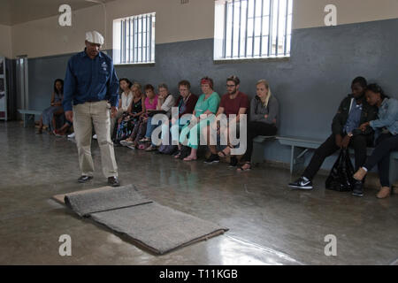 Touristen hören, ein ehemaliger Häftling, der jetzt einen Reiseführer, in eine gemeinsame Zelle auf Robben Island, wo Nelson Mandela während der Apartheid inhaftiert war, Kapstadt. Stockfoto