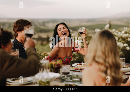 Lächelnde Frau heben Wein Glas und die Unterhaltung mit Freunden zum Abendessen. Gruppe von Menschen, die großartige Zeit im Dinner Party. Stockfoto