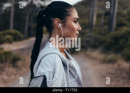 Seitenansicht der jungen Frau mit Kopfhörer stehen im Freien nach Morgen ausgeführt. Weibliche eine Pause nach dem freien Training. Stockfoto