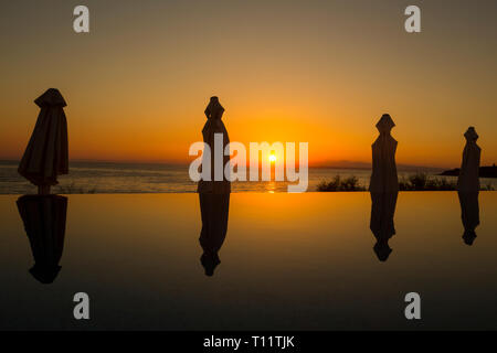 Griechenland, Zakynthos. Sonnenschirme in einem Infinity-pool bei Sonnenaufgang reflektiert. Stockfoto