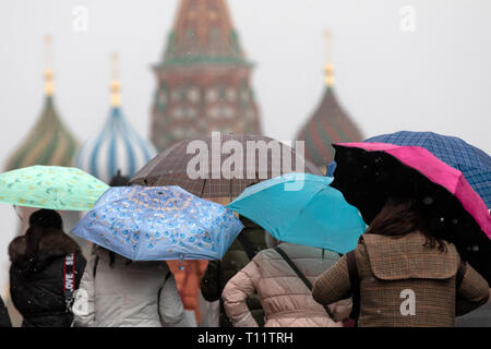 Eine Gruppe von Menschen zu Fuß auf dem Roten Platz unter Regenschirmen in Regen mit Schnee auf dem Hintergrund der Basilius-kathedrale im Zentrum von Moskau, Russland Stockfoto