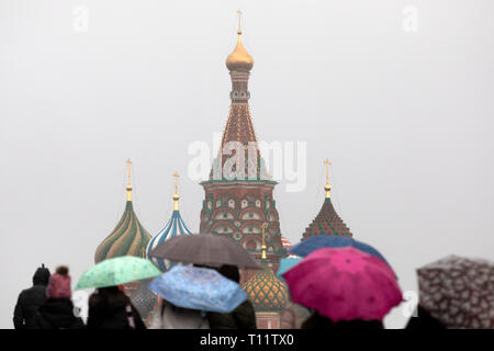 Eine Gruppe von Menschen zu Fuß auf dem Roten Platz unter Regenschirmen in Regen mit Schnee auf dem Hintergrund der Basilius-kathedrale im Zentrum von Moskau, Russland Stockfoto