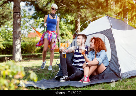 Weibchen bringt Flasche Bier zu Ihren Freunden auf dem Campingplatz im Wald Stockfoto