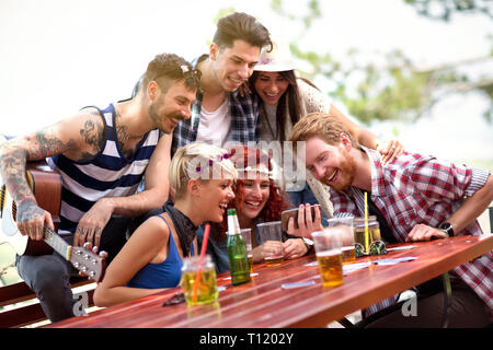 Junges Team in der Natur zu lachen, während sie ihre Fotos auf dem Handy ansehen Stockfoto