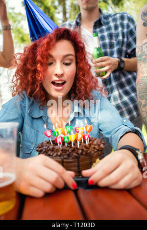 Porträt der jungen Curly rothaarige Mädchen mit kleinen blauen Geburtstag Gap und Schokolade Kuchen in der Natur Stockfoto