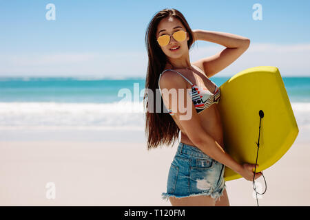 Seitenansicht einer Frau mit einem Bodyboard ihr Urlaub am Strand. Porträt einer Frau in Sonnenbrille am Strand mit einem Bodyboard. Stockfoto