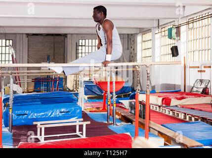 Sportliche afro Mann in Sportswear Übungen am Barren in akrobatischen Hall Stockfoto