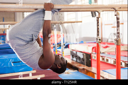 Portrait von afro Mann in Sportswear Übungen am Barren in akrobatischen Hall Stockfoto