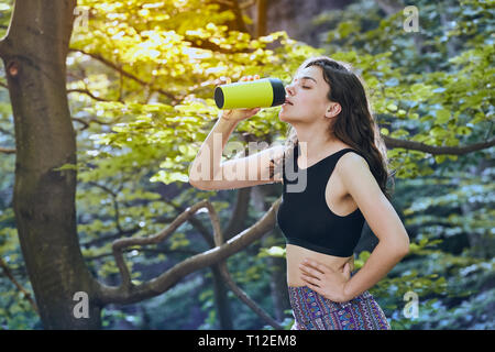 Gesunde Fitness Mädchen Trinkwasser aus grünen Flasche während outdoor Lauftraining in Forest Park im Sommer oder Frühling. Gerne passende Frau. Stockfoto