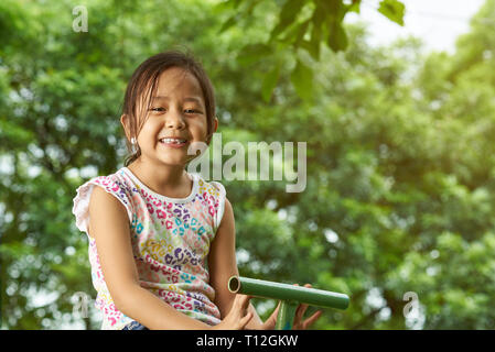 Cute asian kleine Mädchen lächelnd auf die natürlichen sonnigen Hintergrund Stockfoto