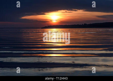 Erstaunlich rot und orange Sonnenuntergang an der Wolga mit der Sonne, die Konturen der Stadt am Horizont und Wolken über dem Wasser Stockfoto