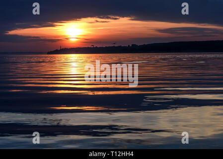 Erstaunlich rot und orange Sonnenuntergang an der Wolga mit der Sonne, die Konturen der Stadt am Horizont und Wolken über dem Wasser Stockfoto