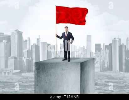 Gut aussehender Geschäftsmann auf der Oberseite der Stadt mit Red Flag Stockfoto