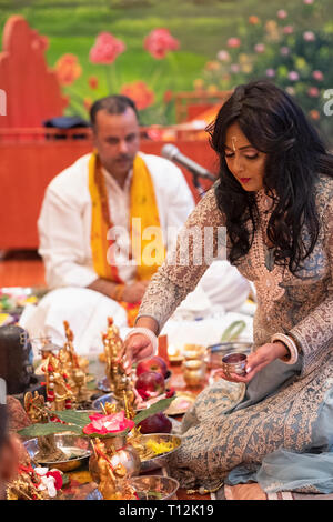 Mit einem pandit hinter ihr sitzt, eine attraktive Hinduistische Frau feiert ihren Geburtstag durch die Unterstützung bei. In Queens, New York. Stockfoto