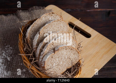 Frisch geschnittenes Stück in der wicker Schüssel auf eine Eiche board mit verstreuten Mehl auf einer hölzernen Hintergrund mit der Leinen. Foto Ansicht von oben. Stockfoto