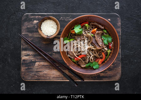 Pfannengerichte mit Soba Nudeln, Fleisch und Gemüse. Asiatische gesundes Essen, gebratene Speisen Schüssel auf schwarzen Hintergrund rühren, Ansicht von oben. Stockfoto