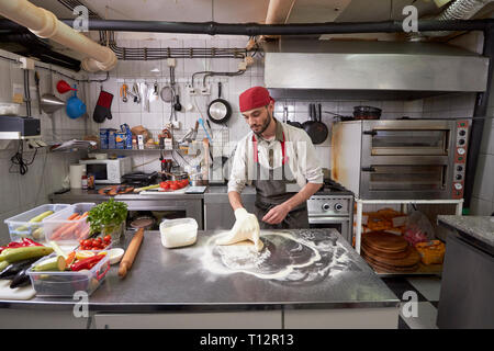 Ein junger Koch, 20-29 Jahre alt, was eine Pizza Teig in eine kommerzielle Küche. Stockfoto