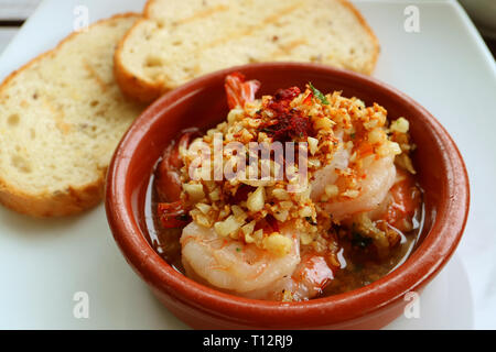 Köstliche Spanische Stil Knoblauch Garnelen oder Gambas al Ajillo mit verschwommenen Geschnitten Brot im Hintergrund Stockfoto