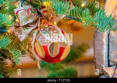 Tand und Bogen am Weihnachtsbaum mit Beleuchtung. Nahaufnahme eines beleuchteten Weihnachtsbaum gegen die Mauer aus Stein und verschwommenen Hintergrund. Reich verzierte Christbaumkugel wit Stockfoto