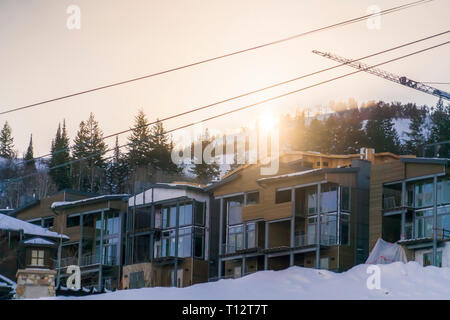Gebäude gegen Berg und Kran in Park City. Fassade der Gebäude in Park City mit der hellen Sonne hinter den schneebedeckten Berge im Hinterg Stockfoto