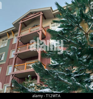 Snowy Nadelbaum gegen Haus mit Balkon in Utah. Einen verschneiten Nadelwald Baum in Park City, Utah im Winter. Ein Gebäude mit kleinen Balkonen gegen Blue sk Stockfoto