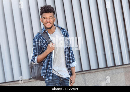 Junge afrikanische amerikanische Mann, der Rucksack steht isoliert auf Stadt Straße Kamera lächelt Fröhlich Stockfoto