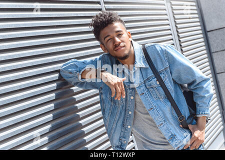 Junge afrikanische amerikanische Mann auf der Straße an der Wand gelehnt, die Kamera lächelnd verspielt Stockfoto