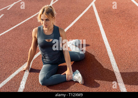 Sportlicher Lifestyle. Junge Frau auf Stadion sitzen am Anschluss stretching Beine nachdenklich Stockfoto