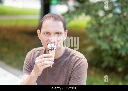 Mann das Essen ein Schoko Vanille Eis gelato Kegel mit bokeh Hintergrund der Park in Europa City während der sonnigen Sommertag Stockfoto
