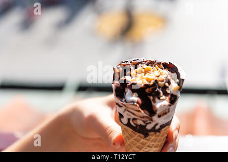 Hand eine Weiße Vanille Schokolade swirl Eis gelato Kegel mit bokeh Hintergrund an heissen Sommertag und Erdnüsse nachfüllen Stockfoto