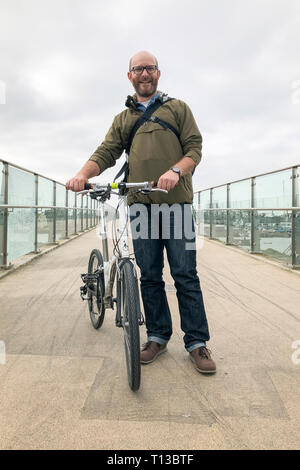 Ein weißer Mann steht auf dem Shoreham Adur Ferry Bridge mit einem faltrad Stockfoto