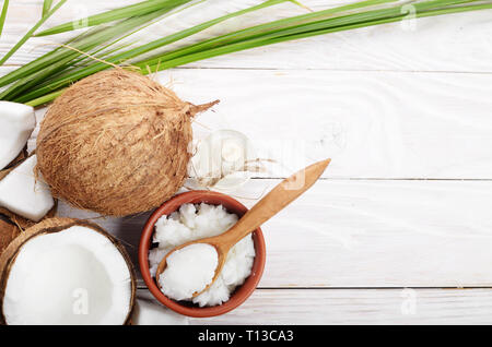 Flach Hintergrund der Kokosnuss, Kokosnussschalen, Öl in Ton Schüssel und Glas Glas und Löffel auf weiße Holztisch Stockfoto