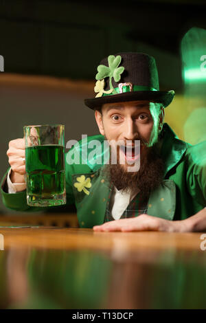 Dunkelhaarige bärtiger junger Mann in einem Kobold hut mit Shamrock suchen begeistert Stockfoto