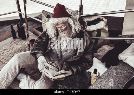 Obdachlose alte Mann lesen Buch fand er mit Begeisterung. Stockfoto
