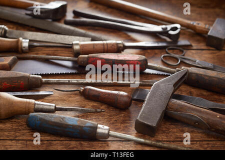 Alte hölzerne behandelt Werkzeuge für die Holzbearbeitung mit Schraubendreher, Hammer oder Hammer, Meißel und Schere in einem hohen Winkel auf einem rustikalen, mit Holz Werkbank Stockfoto
