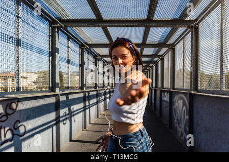 Portrait von lächelnden jungen Frau mit Ohrhörern auf einer Brücke erreichen, die ihre Hand Stockfoto