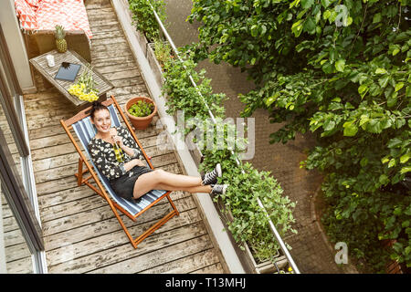 Junge Frau im Liegestuhl sitzen, entspannen Sie auf Ihrem Balkon Stockfoto