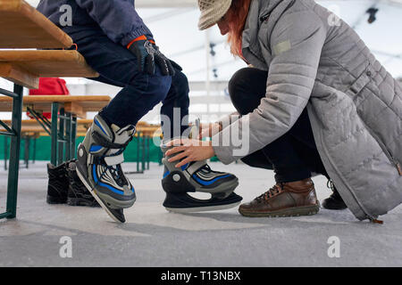 Mutter helfen ihr Sohn Schlittschuhe anziehen Stockfoto