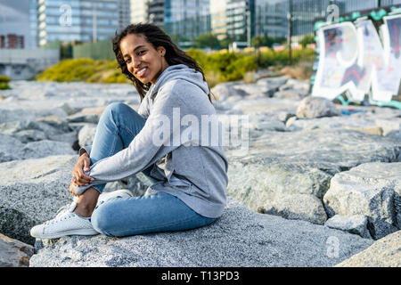 Junge Frau sitzen auf den Felsen am Strand, entspannend Stockfoto
