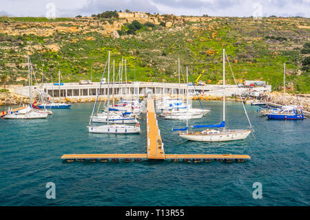 MGARR, Gozo, Malta - Februar 02, 2013 - Blick auf die Boote im Hafen mit Ferienwohnungen am Hang auf die hintere und die Menschen über ihre Busines gehen Stockfoto