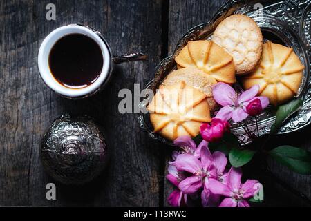 Lecker Kaffee in einer traditionellen türkischen Cup und Butter cookies und einem Zweig rosa Blumen auf einem Holztisch - Flach essen Hintergrund Stockfoto